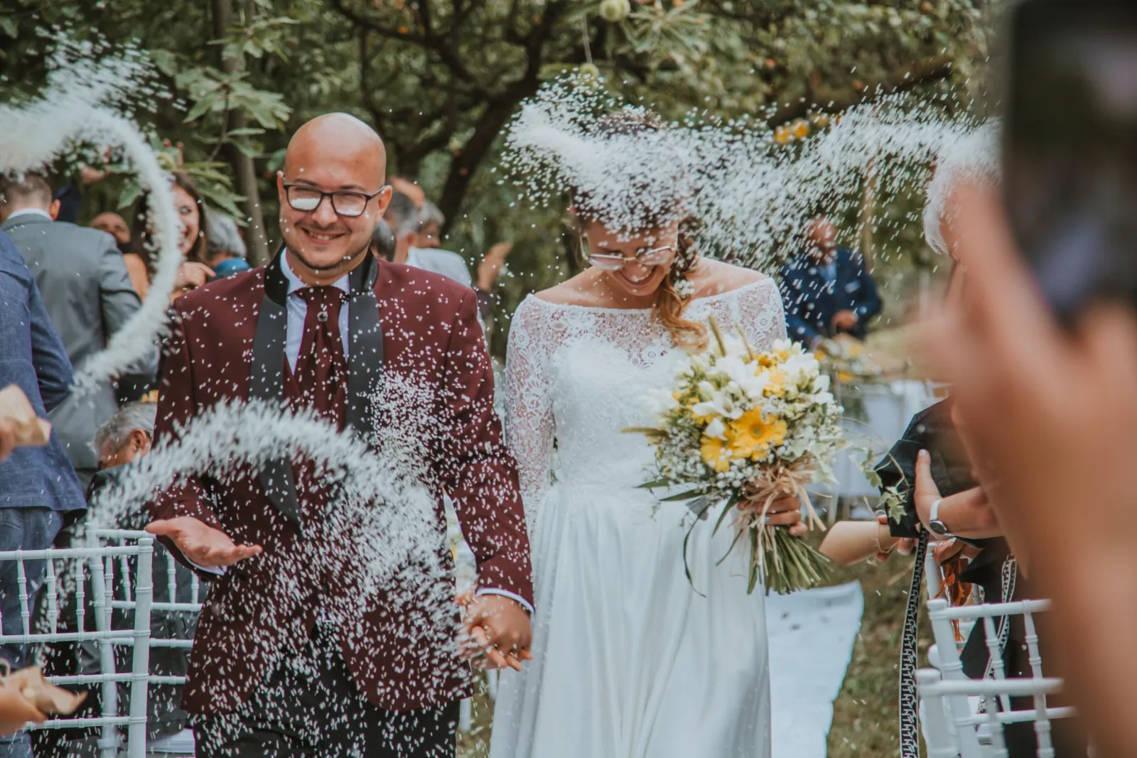 Gli sposi sorridono sotto il lancio del riso, circondati dagli invitati